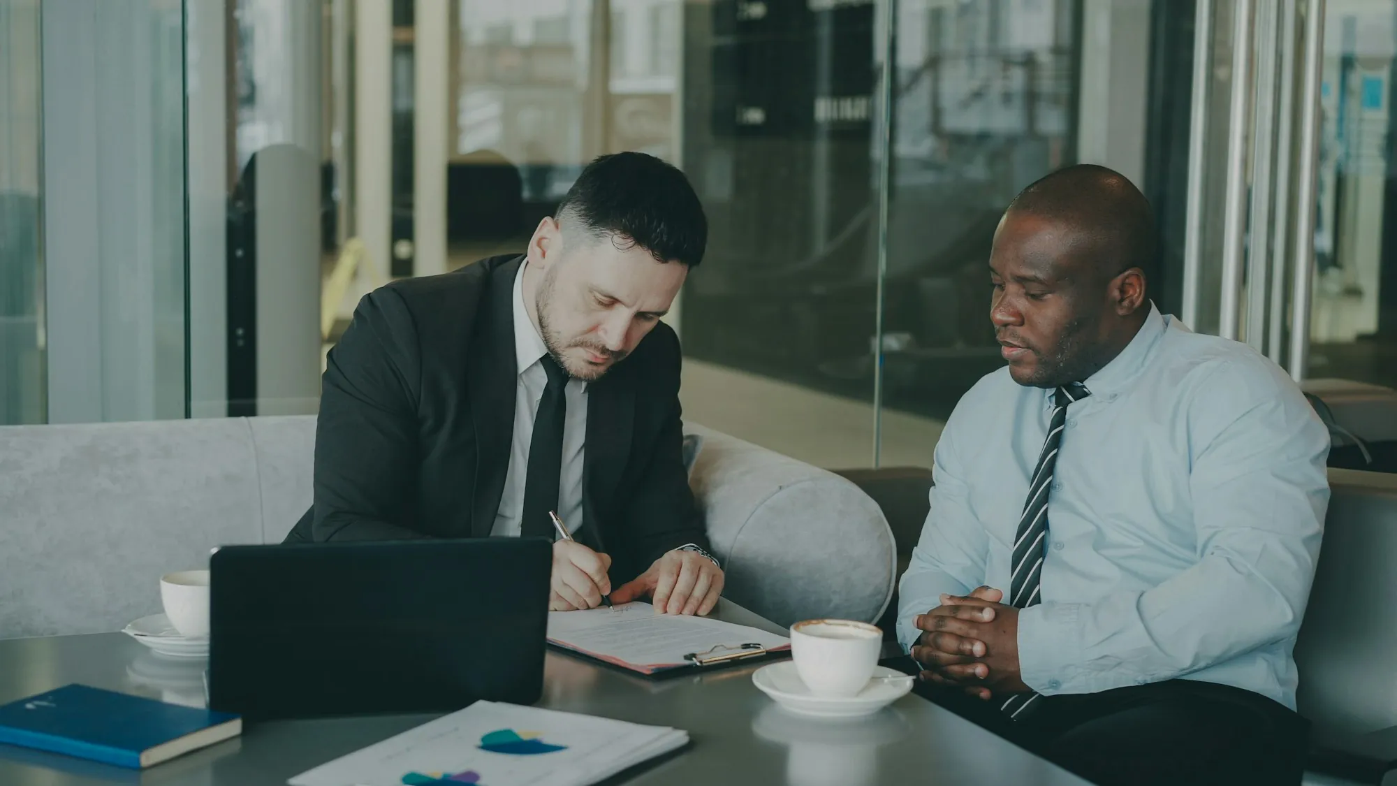 Two men reviewing paperwork with a laptop at a meeting